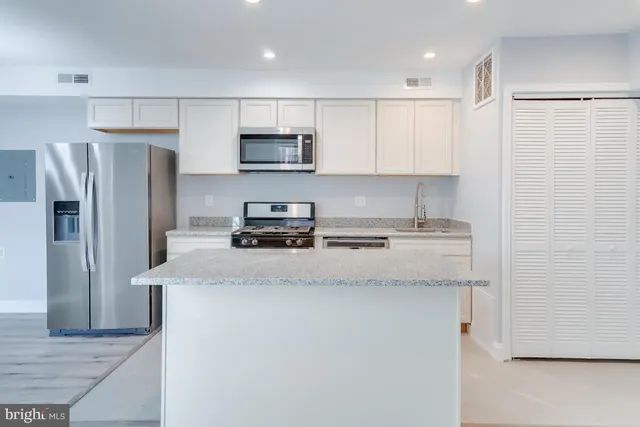 a kitchen with stainless steel appliances granite countertop a refrigerator a stove a sink a microwave and white cabinets with wooden floor