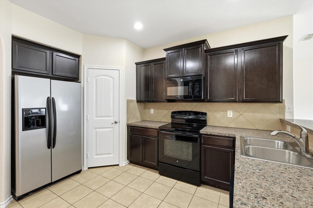 720 Rio Bravo Drive Fort Worth, TX 76052 - Photo 17 of 38 Kitchen featuring dark wood-finish cabinetry, stainless steel side-by-side refrigerator, black electric range with microwave, tile flooring, and laminate countertops