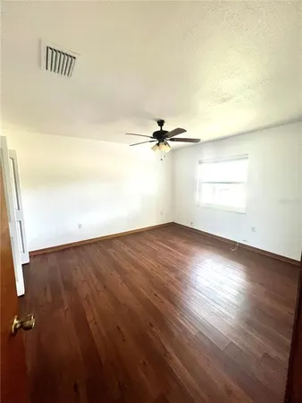 an empty room with wooden floor fan and windows