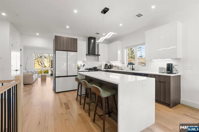 a kitchen with stainless steel appliances kitchen island granite countertop a refrigerator a sink a stove and white cabinets with wooden floor