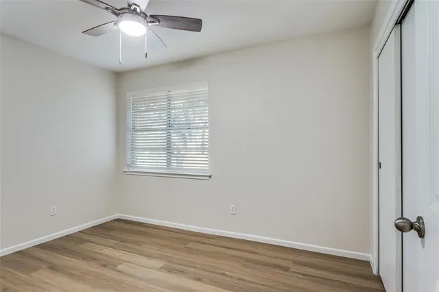 an empty room with wooden floor fan and windows