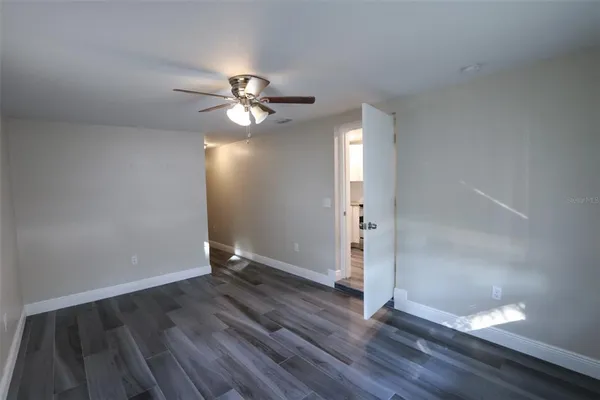 an empty room with wooden floor chandelier fan and windows