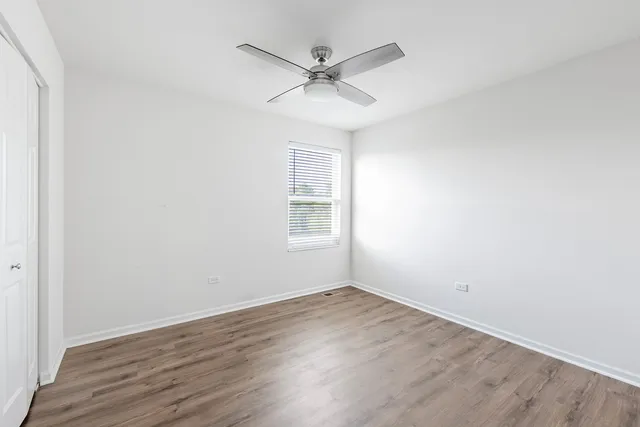 an empty room with wooden floor ceiling fan and windows