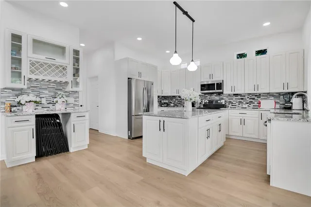 a kitchen with kitchen island granite countertop a stove a sink a refrigerator and white cabinets with wooden floor