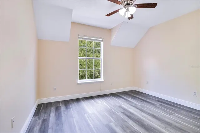 an empty room with wooden floor chandelier fan and windows