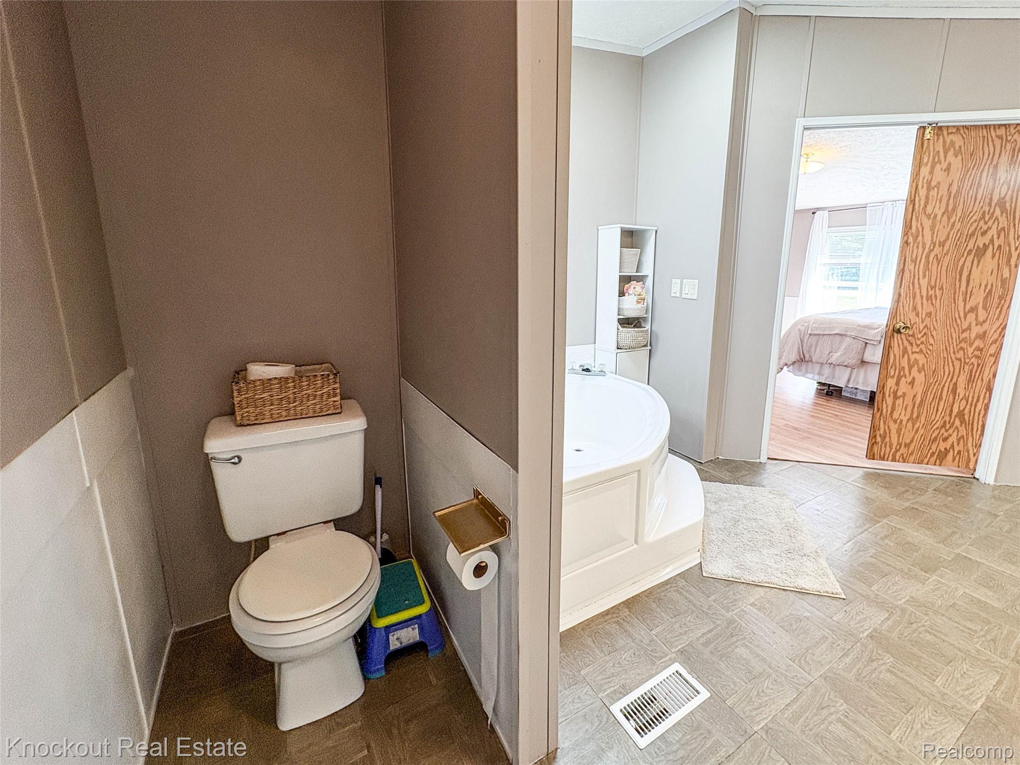 7760 Bell Road Birch Run, MI 48415 - Photo 34 of 68 Spacious bathroom featuring a built-in corner soaking tub, neutral-toned walls with wainscoting, and wood-finish flooring