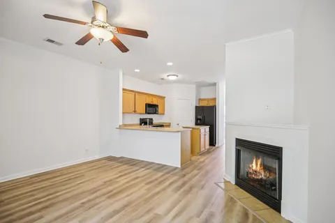 a view of a livingroom with wooden floor a ceiling fan and kitchen space