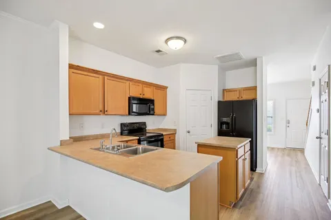 a kitchen with stainless steel appliances a stove top oven a sink a refrigerator white cabinets and wooden floor