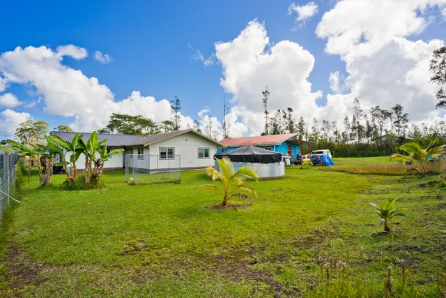 a view of yellow house with swimming pool lawn chairs and plants