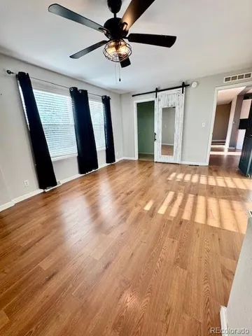a view of an empty room with wooden floor and a ceiling fan