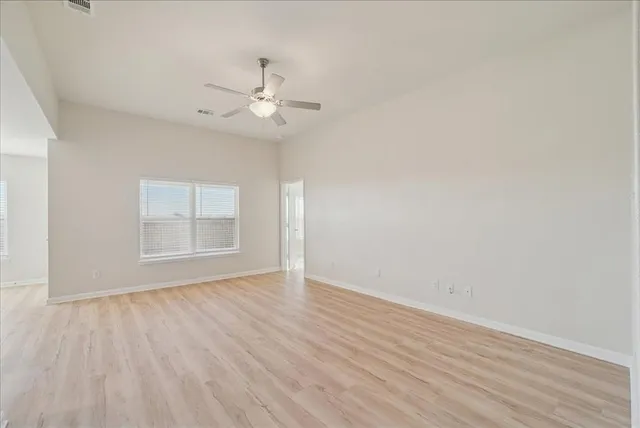 an empty room with wooden floor fan and windows