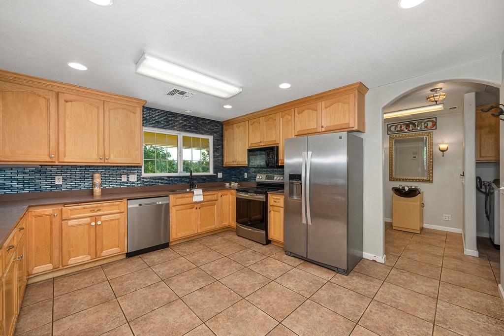 6181 Lambert Lane El Dorado, CA 95623 - Photo 29 of 68 kitchen with stainless steel appliances, arched walkways, dark countertops, backsplash, and light tile patterned flooring