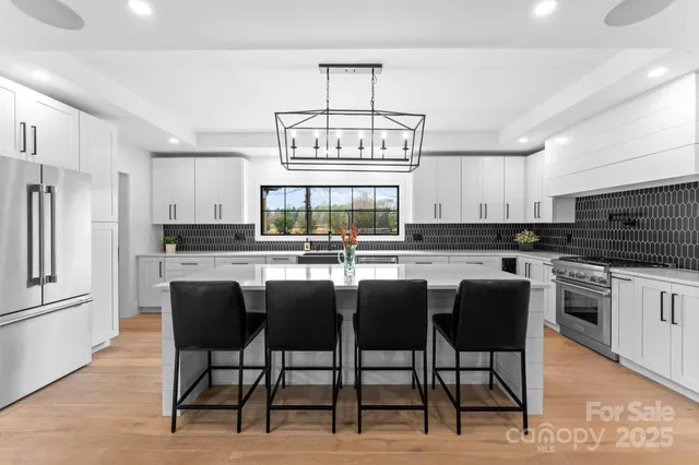 a kitchen with stainless steel appliances granite countertop a stove top oven a refrigerator a sink and a dining table with white cabinets