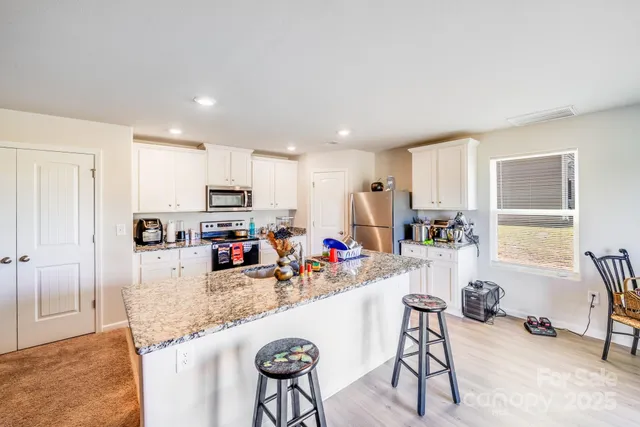 a kitchen with stainless steel appliances granite countertop a refrigerator a stove a sink a dining table and chairs with wooden floor