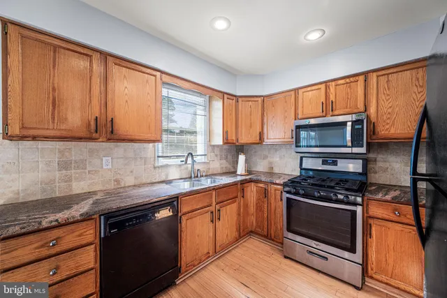 a kitchen with stainless steel appliances kitchen island granite countertop a refrigerator a oven a sink with wooden cabinets and wooden floor