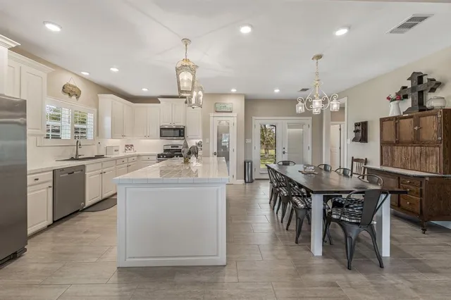 a kitchen with stainless steel appliances kitchen island granite countertop a dining table chairs and white cabinets