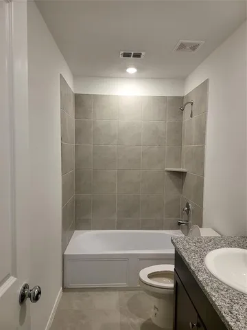 a bathroom with a granite countertop bathtub shower sink vanity and toilet