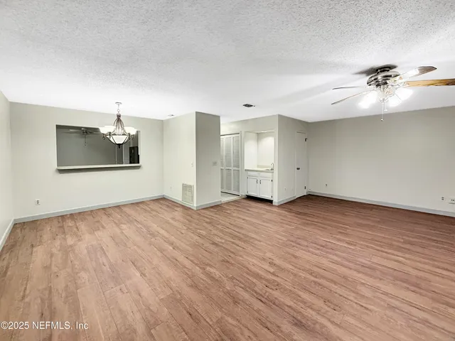 an empty room with wooden floor chandelier fan and windows