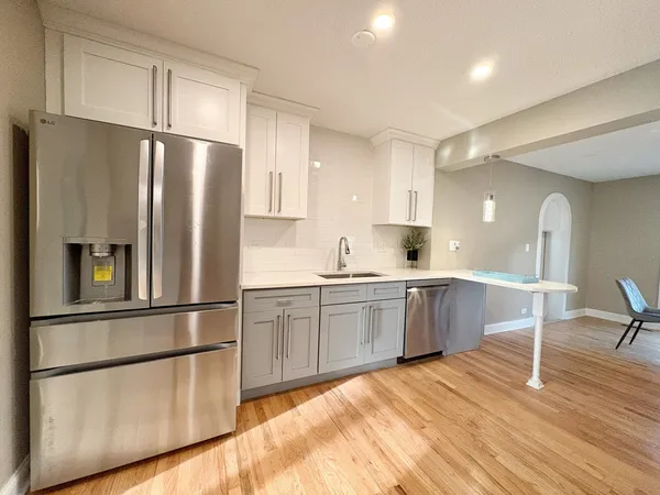 a kitchen with granite countertop a refrigerator a sink dishwasher a stove and white cabinets with wooden floor
