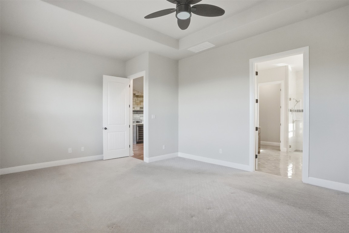 1441 River Vista Road Georgetown, TX 78628 - Photo 22 of 37 Unfurnished bedroom with light carpet, ceiling fan, a raised ceiling, beverage cooler, and connected bathroom