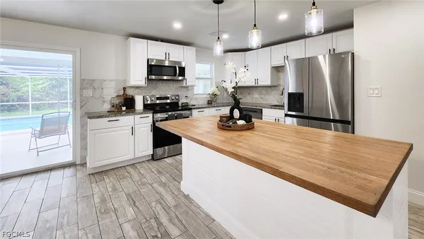 a kitchen with stainless steel appliances granite countertop a stove top oven a refrigerator a sink and white cabinets with wooden floor
