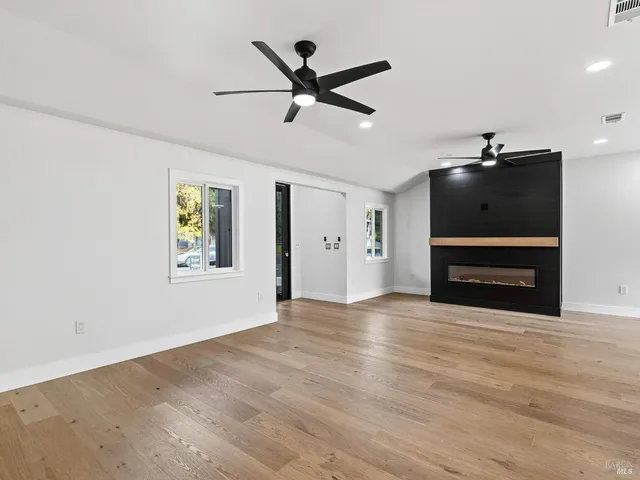 a view of an empty room with wooden floor a fireplace and a window
