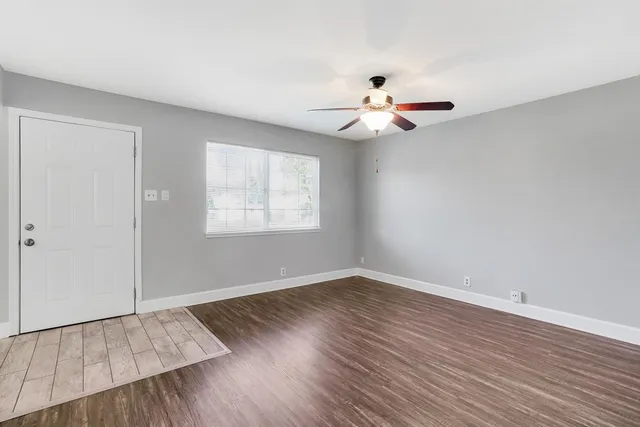 an empty room with wooden floor chandelier fan and windows