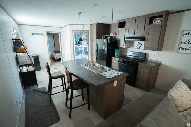 2491 Highway 89, Unit 111 Pleasant View, UT 84404 - Photo 6 of 20 Kitchen featuring dark countertops, black appliances, washer and clothes dryer, a kitchen bar, and an island with sink