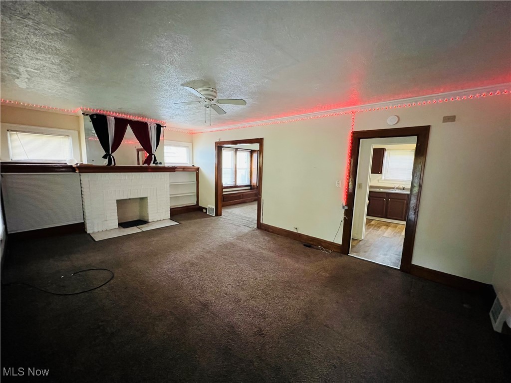 968 Whitby Road Cleveland Heights, OH 44112 - Photo 2 of 19 Unfurnished living room with dark colored carpet, a ceiling fan, a textured ceiling, a brick fireplace, and ornamental molding