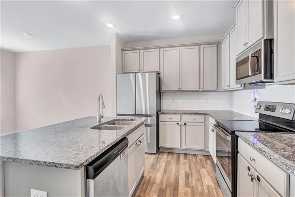 a kitchen with kitchen island granite countertop stainless steel appliances a refrigerator a stove top oven and wooden floors