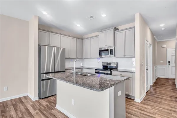 a kitchen with stainless steel appliances granite countertop a refrigerator a sink a stove and white cabinets with wooden floor