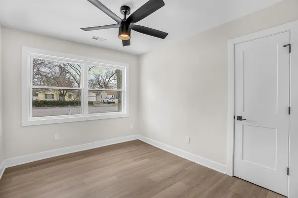 an empty room with wooden floor ceiling fan and windows