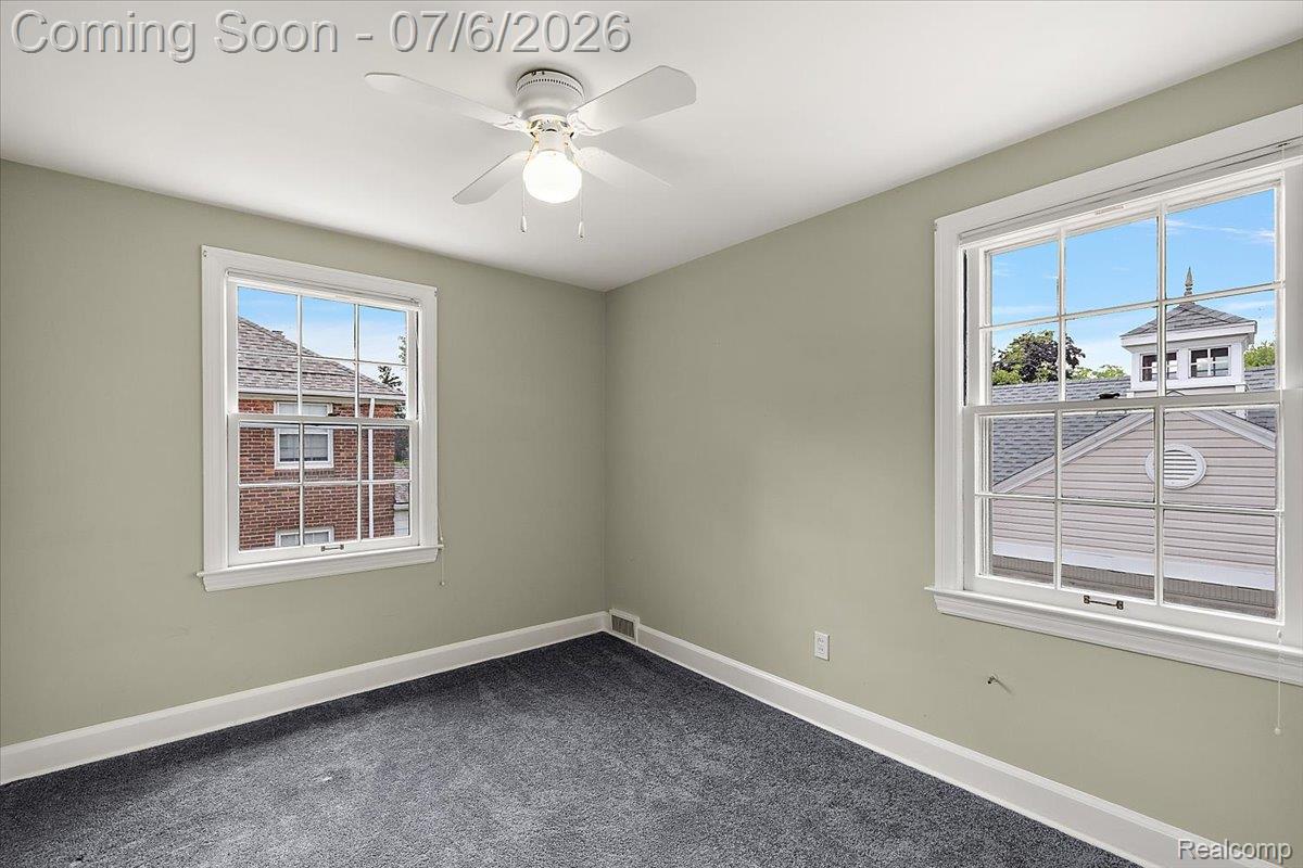 1051 Devonshire Road Grosse Pointe, MI 48230 - Photo 43 of 98 Room featuring two double-hung windows with white trim, a ceiling fan with light fixture, light gray walls, and dark gray carpet flooring
