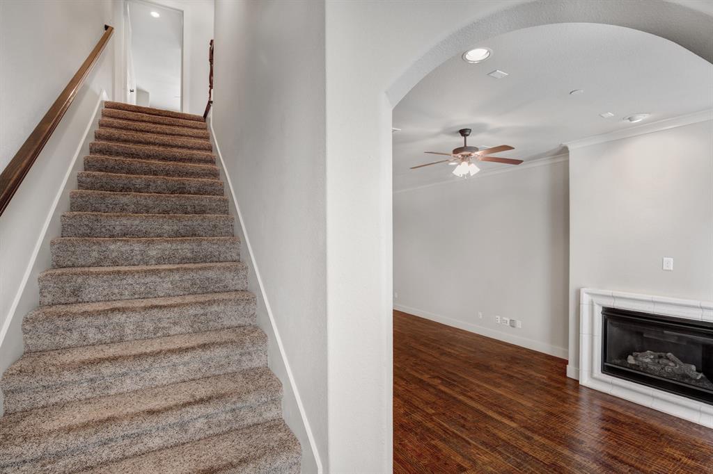 4111 Rawlins Street, Unit 403 Dallas, TX 75219 - Photo 11 of 23 Carpeted staircase with wood handrail, featuring an arched entryway opening to a room with wood-finish flooring, a white mantel fireplace, and a ceiling fan