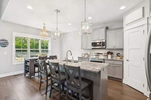 a kitchen with stainless steel appliances granite countertop a stove a refrigerator a kitchen island a dining table and chairs with wooden floor