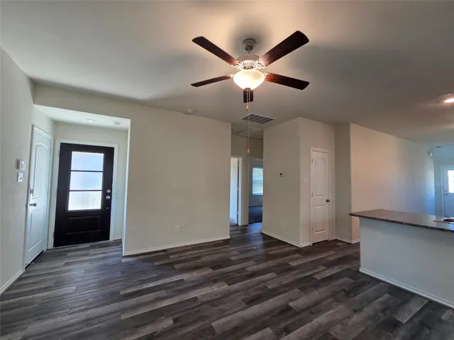 a view of an empty room with wooden floor and a ceiling fan