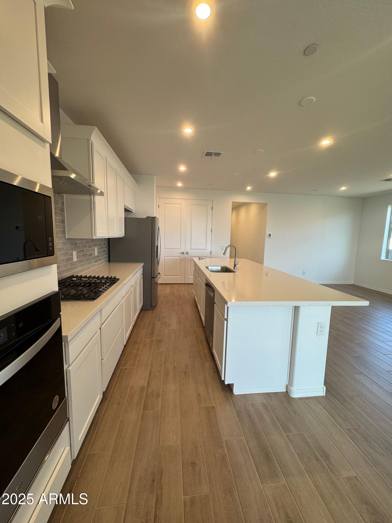 13351 West Eagle Feather Road Peoria, AZ 85383 - Photo 5 of 23 a large kitchen with stainless steel appliances a large counter top a stove and a wooden floors