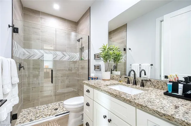 a bathroom with a granite countertop sink a toilet a mirror and shower