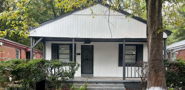 a view of small white house with large windows and a small yard