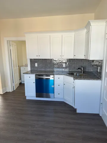 a kitchen with stainless steel appliances granite countertop a stove a sink and white cabinets with wooden floor