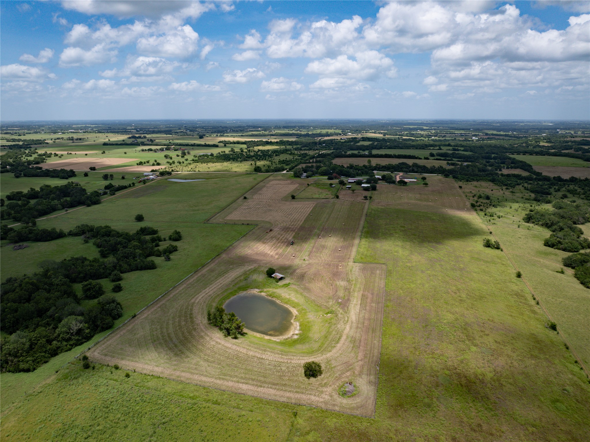 1281 Post Oak Point Road New Ulm, TX 78950 - Photo 27 of 29 Vast green acreage featuring a tranquil pond and agricultural fields beneath a wide-open sky.