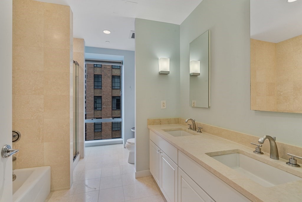 80 Broad Street, Unit 1002 Boston, MA 02110 - Photo 9 of 16 a bathroom with a double vanity sink a mirror and a bathtub
