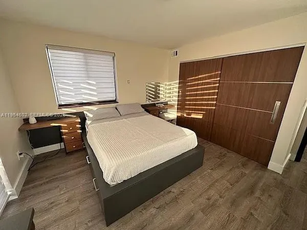 a bedroom with a bed and dresser with wooden floor