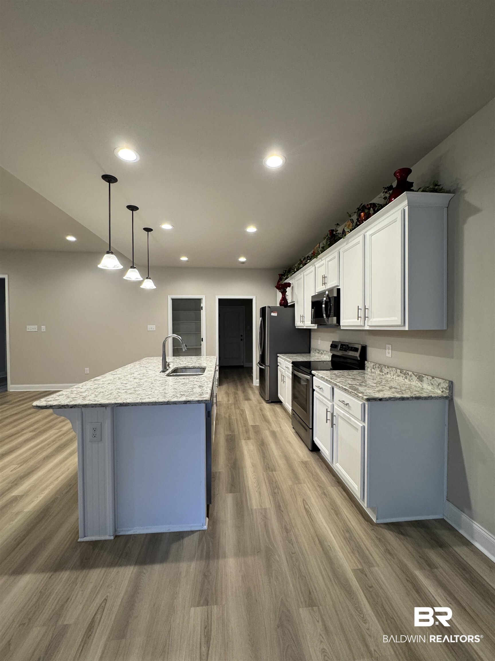 1060 Chloe Street Foley, AL 36535 - Photo 12 of 28 Open-concept kitchen featuring an elongated central island with an undermount sink, granite-style countertops, white cabinetry, and wood-finish flooring