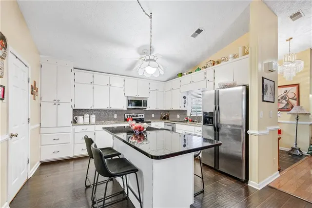 a room with stainless steel appliances kitchen island granite countertop a table chairs and a view of living room