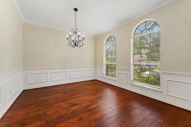 an empty room with wooden floor chandelier and windows