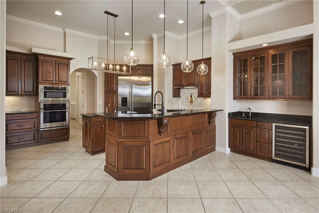 5669 Sago Court Naples, FL 34119 - Photo 9 of 41 Kitchen with arched walkways, glass insert cabinets, beverage cooler, decorative backsplash, and crown molding