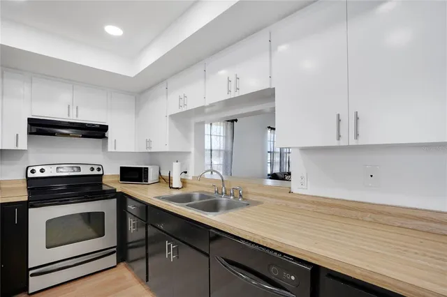 a kitchen with a sink dishwasher stove and white cabinets with wooden floor