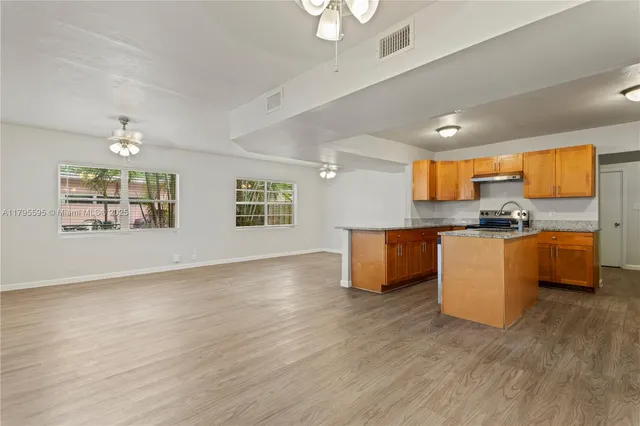 a kitchen with kitchen island granite countertop a stove top oven a sink a counter space and cabinets