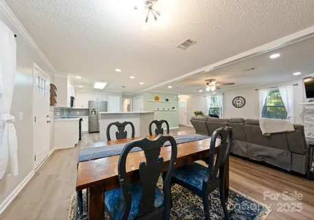 a view of a dining room and livingroom with furniture wooden floor a rug a painting and a chandelier